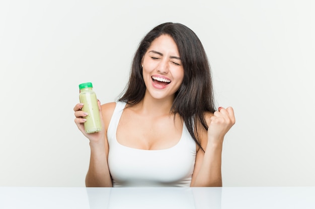 Joven mujer hispana sosteniendo una bebida vegetal animando despreocupado y emocionado.