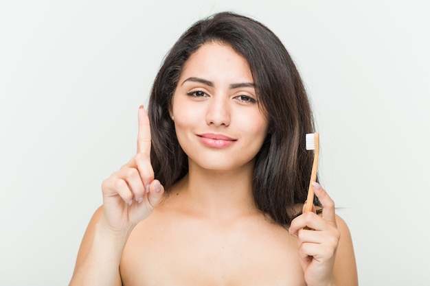 Joven mujer hispana sosteniendo un cepillo de dientes mostrando el número uno con el dedo.