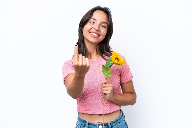 Joven mujer hispana sosteniendo girasol aislado en fondo blanco haciendo el gesto de venir