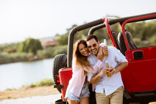 Joven mujer y hombre divirtiéndose al aire libre cerca de coche rojo en día de verano