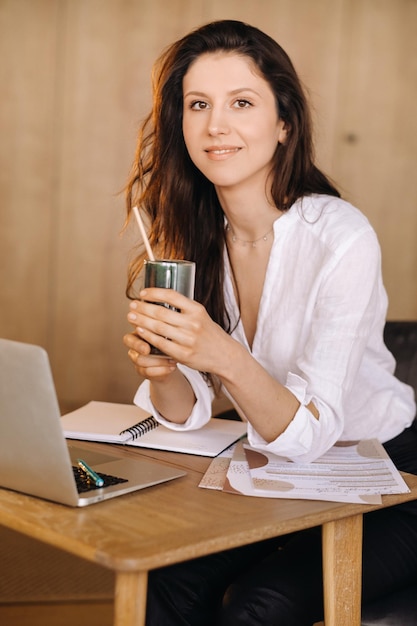 Una joven mujer independiente con un cóctel en las manos en su lugar de trabajo