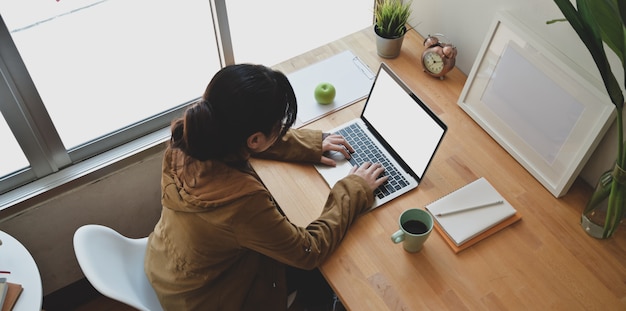 Joven mujer independiente escribiendo en la computadora portátil de pantalla en blanco