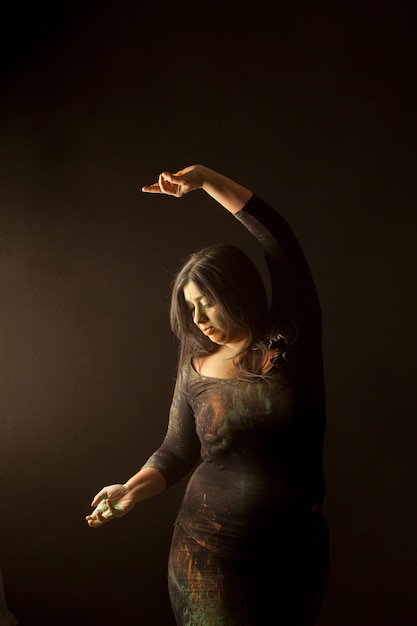 Joven mujer india aislada bailando y jugando con polvo de color en ropa oscura