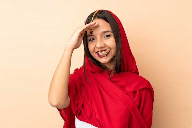 Joven mujer india aislada en la pared de color beige saludando con la mano con expresión feliz