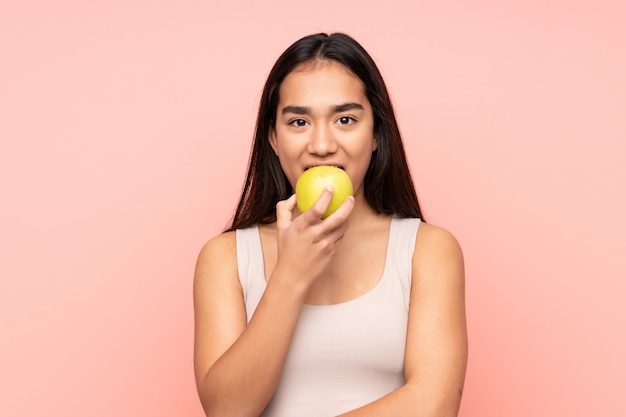 Joven mujer india aislada en la pared rosa comiendo una manzana