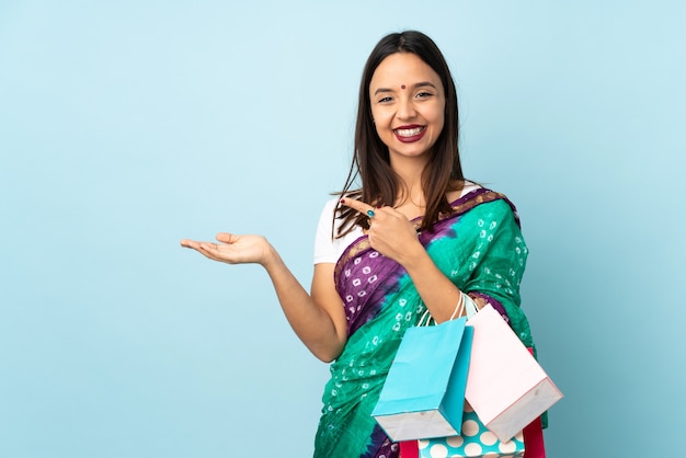 Joven mujer india con bolsas de compras con copyspace imaginario en la palma para insertar un anuncio