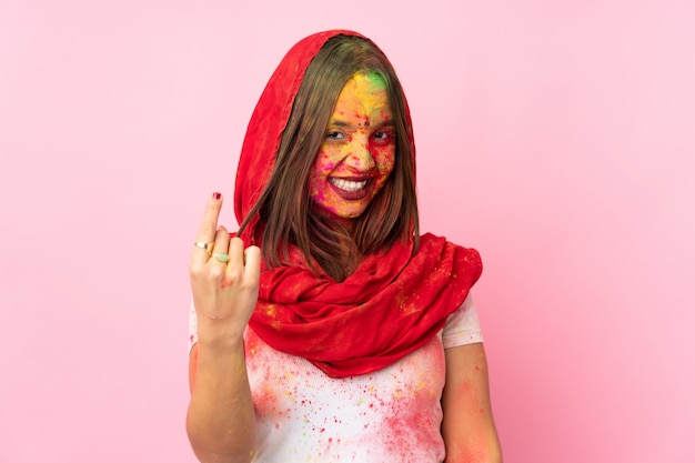 Joven mujer india con coloridos polvos de holi en su rostro aislado en la pared rosa haciendo gesto que viene