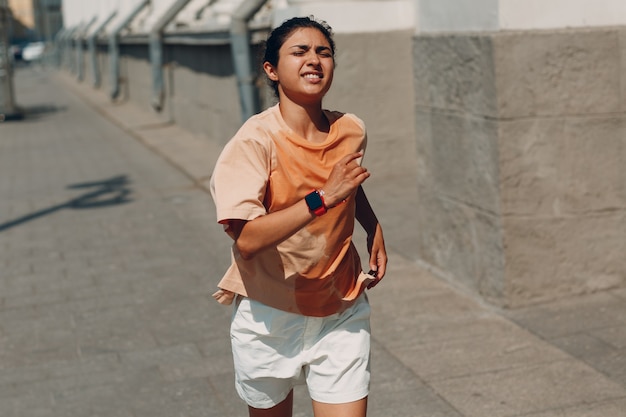 Joven mujer india corredor trotar en camiseta sudorosa mojada en las calles de la ciudad