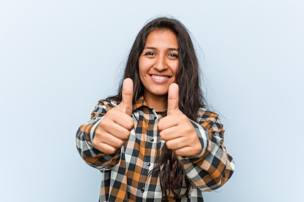 Joven mujer india fresca con pulgares arriba, aplausos sobre algo