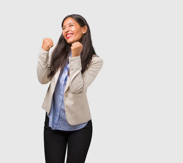 Joven mujer india de negocios muy feliz y emocionada, alzando los brazos, celebrando una victoria o éxito, ganando la lotería