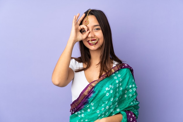 Joven mujer india en la pared de color púrpura que muestra bien firmar con los dedos