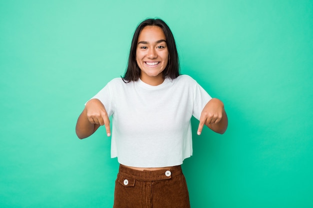 Joven mujer india de raza mixta aislada apunta hacia abajo con los dedos, sentimiento positivo.