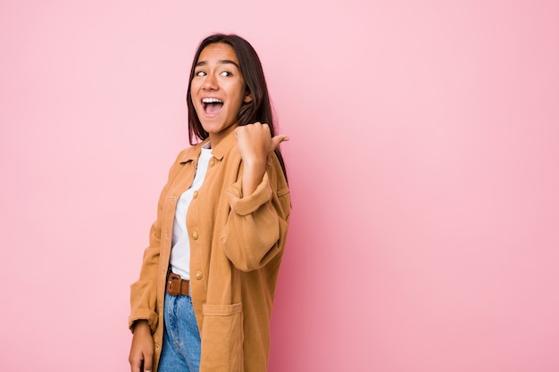 Joven mujer india de raza mixta puntos aislados con el dedo pulgar, riendo y sin preocupaciones.