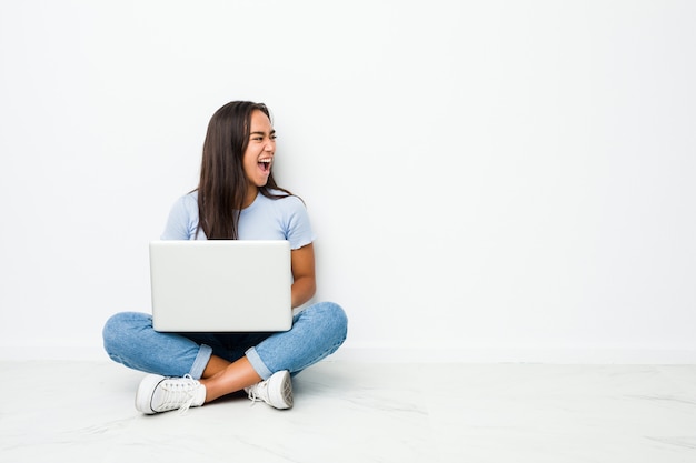 Joven mujer india de raza mixta sentada trabajando en la computadora portátil gritando hacia un espacio de copia