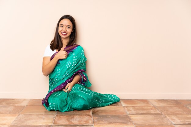 Joven mujer india sentada en el suelo dando un gesto de pulgares arriba