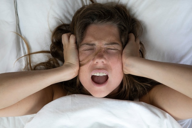 Joven mujer infeliz deprimida acostada en la cama con problemas de salud gritando