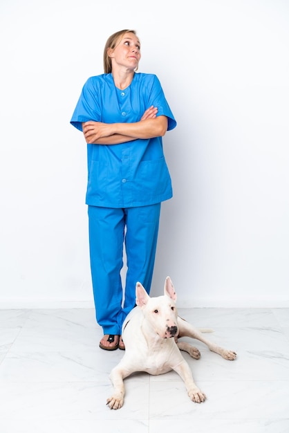 Joven mujer inglesa veterinaria con perro aislado sobre fondo blanco haciendo gesto de dudas mientras levanta los hombros