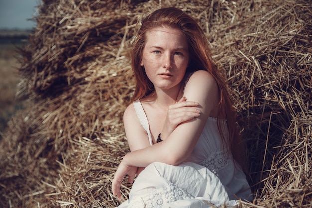 Joven mujer de jengibre en el campo de trigo con aspecto relajado. Hembra en un campo agrícola durante la puesta de sol.