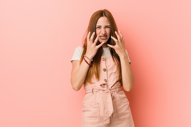 Joven mujer de jengibre con pecas molesto gritando con las manos tensas.