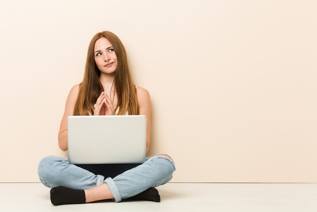 Joven mujer de jengibre sentado en el piso de su casa haciendo un plan en mente, creando una idea.