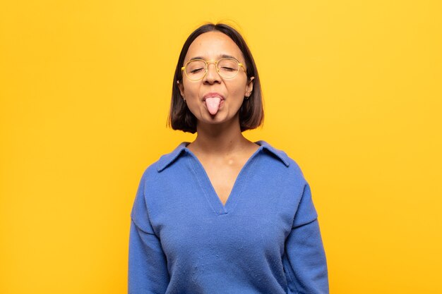 Joven mujer latina con actitud alegre, despreocupada y rebelde, bromeando y sacando la lengua, divirtiéndose