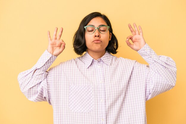 Joven mujer latina aislada sobre fondo amarillo se relaja después de un duro día de trabajo, ella está realizando yoga.