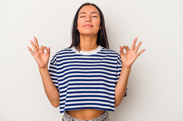 Joven mujer latina aislada sobre fondo blanco se relaja después de un duro día de trabajo, ella está realizando yoga.