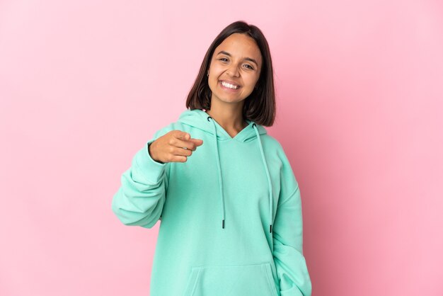 Joven mujer latina aislada sobre fondo rosa apuntando al frente con expresión feliz