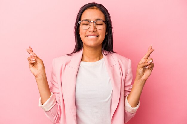 Joven mujer latina aislada sobre fondo rosa cruzando los dedos para tener suerte