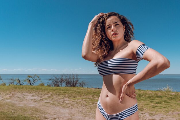 Joven mujer latina blanca en la playa posando mirando hacia arriba con cara confundida