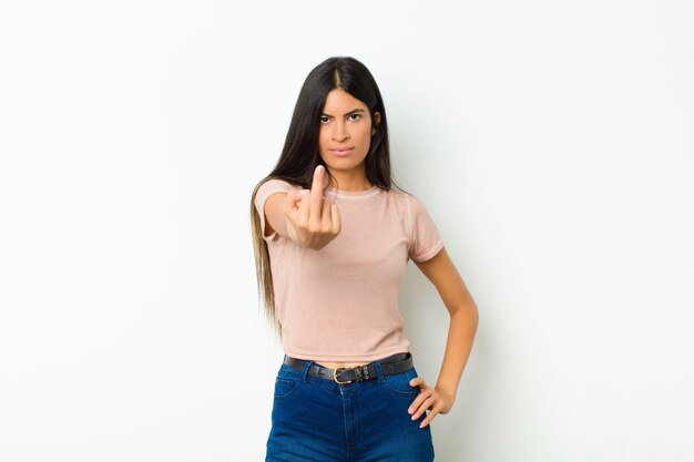 Joven mujer latina bonita que se siente enojada, molesta, rebelde y agresiva, moviendo el dedo medio, luchando contra la pared plana