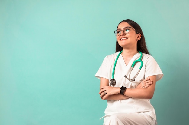 Joven mujer latina feliz con gafas y un estetoscopio usa uniforme de medicina de brazos cruzados.