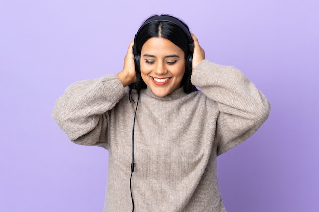 Joven mujer latina en pared púrpura escuchando música