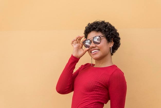 Una joven mujer latina posando y sonriendo frente a la pared naranja con gafas de sol Panamá