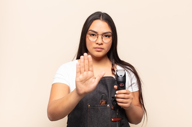 Joven mujer latina que parece seria, severa, disgustada y enojada mostrando la palma abierta haciendo gesto de parada