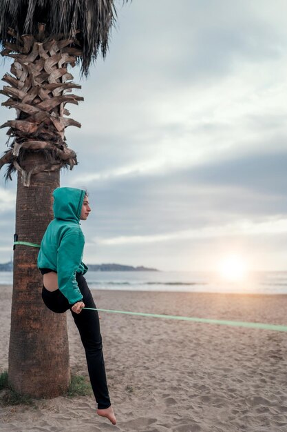 Joven mujer latina sentada y balanceándose en el yoga del forro flojo de las correas en la playa de La Serena