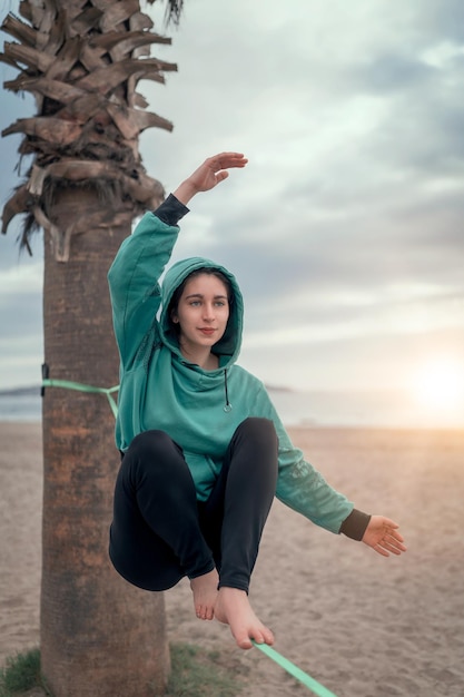 Joven mujer latina sentada y balanceándose en el yoga slacklining de las correas en la playa de La Serena