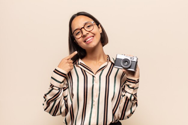 Joven mujer latina sonriendo con confianza apuntando a su propia sonrisa amplia, actitud positiva, relajada y satisfecha