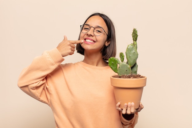 Joven mujer latina sonriendo con confianza apuntando a su propia sonrisa amplia, actitud positiva, relajada y satisfecha