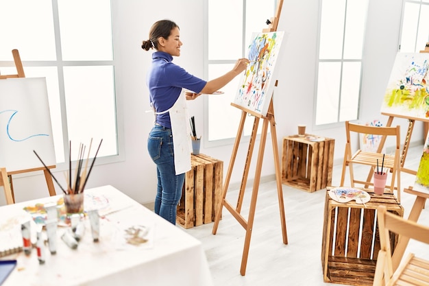 Joven mujer latina sonriendo dibujo confiado en el estudio de arte