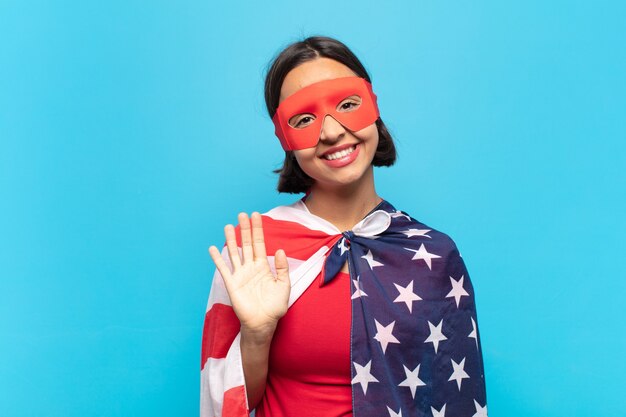 Joven mujer latina sonriendo feliz y alegremente, saludando con la mano, dándote la bienvenida y saludándote, o despidiéndote