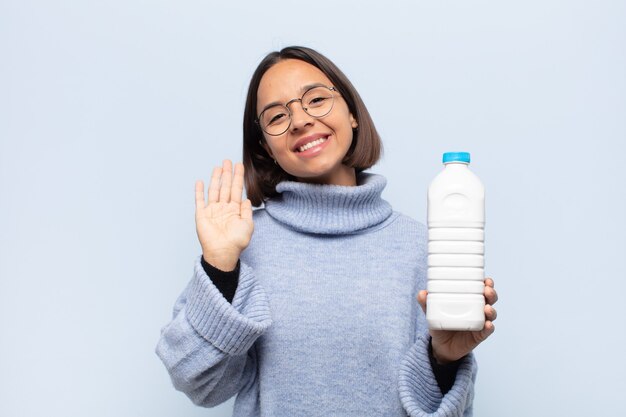 Joven mujer latina sonriendo feliz y alegremente, saludando con la mano, dándote la bienvenida y saludándote, o diciéndote adiós