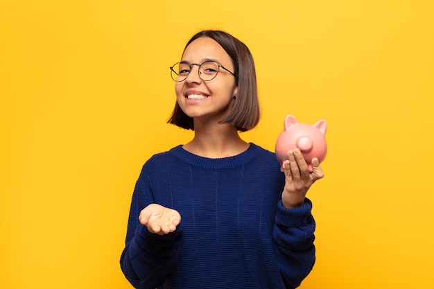 Joven mujer latina sonriendo felizmente con una mirada amable, segura y positiva, ofreciendo y mostrando un objeto