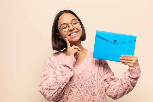 Joven mujer latina sonriendo felizmente y soñando despierto o dudando, mirando hacia el lado