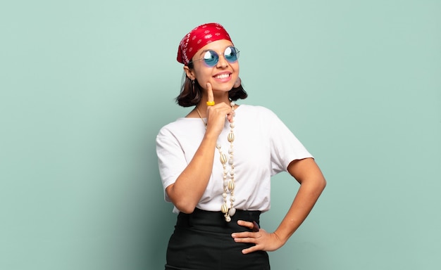 Joven mujer latina sonriendo felizmente y soñando despierto o dudando, mirando hacia el lado