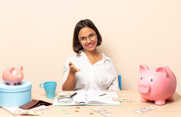 Foto joven mujer latina sonriendo, luciendo feliz, confiada y amigable, ofreciendo un apretón de manos para cerrar un trato, cooperando