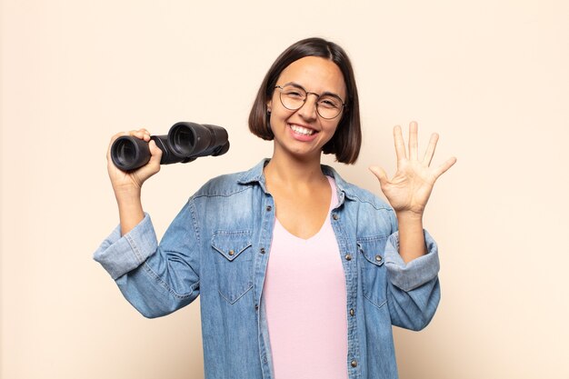 Joven mujer latina sonriendo y mirando amistosamente, mostrando el número cinco o quinto con la mano hacia adelante, contando hacia atrás