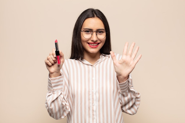 Joven mujer latina sonriendo y mirando amistosamente, mostrando el número cinco o quinto con la mano hacia adelante, contando hacia atrás