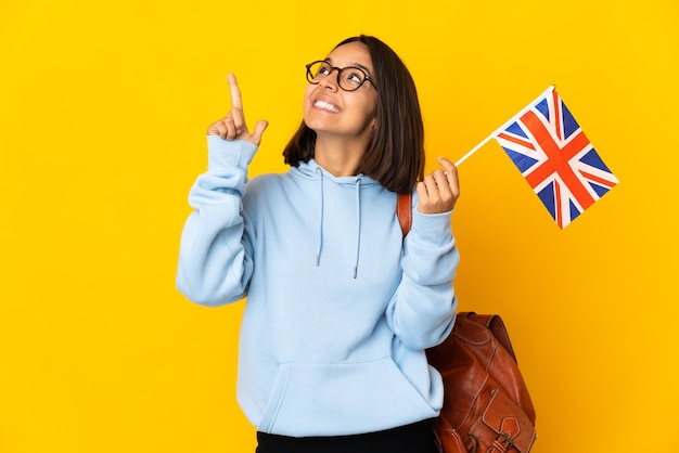 Joven mujer latina sosteniendo una bandera del Reino Unido aislada sobre fondo amarillo apuntando con el dedo índice una gran idea