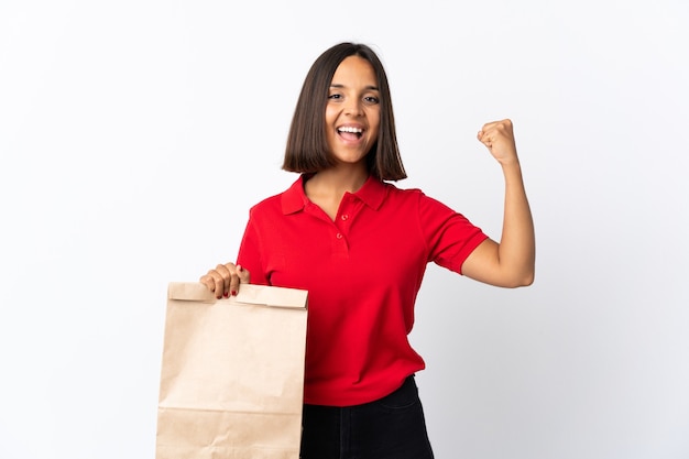 Joven mujer latina sosteniendo una bolsa de compras aislada en blanco haciendo un gesto fuerte